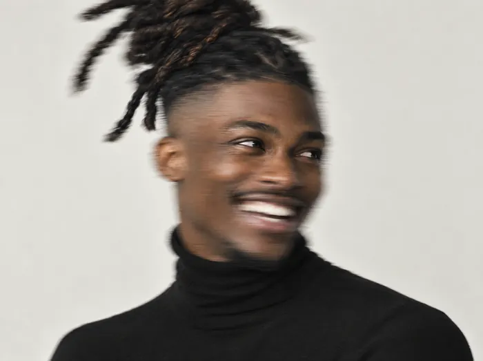 Jamal, a barber with tied-up locs and shaved sides, laughing, his head a soft blur