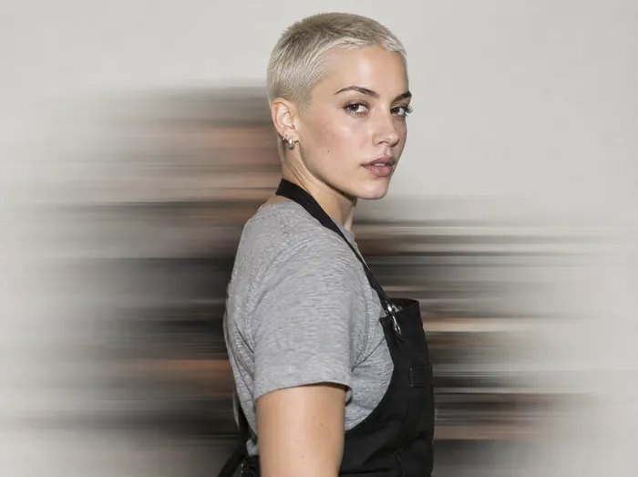 Noor, a barber with a platinum buzz cut in a black apron, mid-turn in a horizontal blur