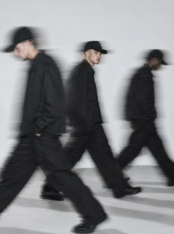 Three barbers dressed in black walk past the camera in a long-exposure blur